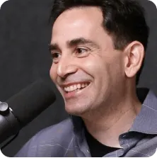 Man smiling and speaking into a microphone against a dark background.
